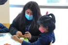 A graduate student volunteer helps a Westminster student make a parachute out of tissue paper, string, pipe-cleaners and paper cups.