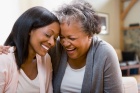 Photo of older mother with her adult child, leaning with their heads together while sitting. 