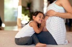 Photo of a small female child, pressing her ear against her mother's pregnant belly. 