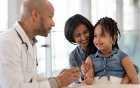 Male provider in exam room, talking with a mother and female child. 