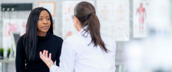 Female patient sitting on an exam table talking with a female medical provider.
